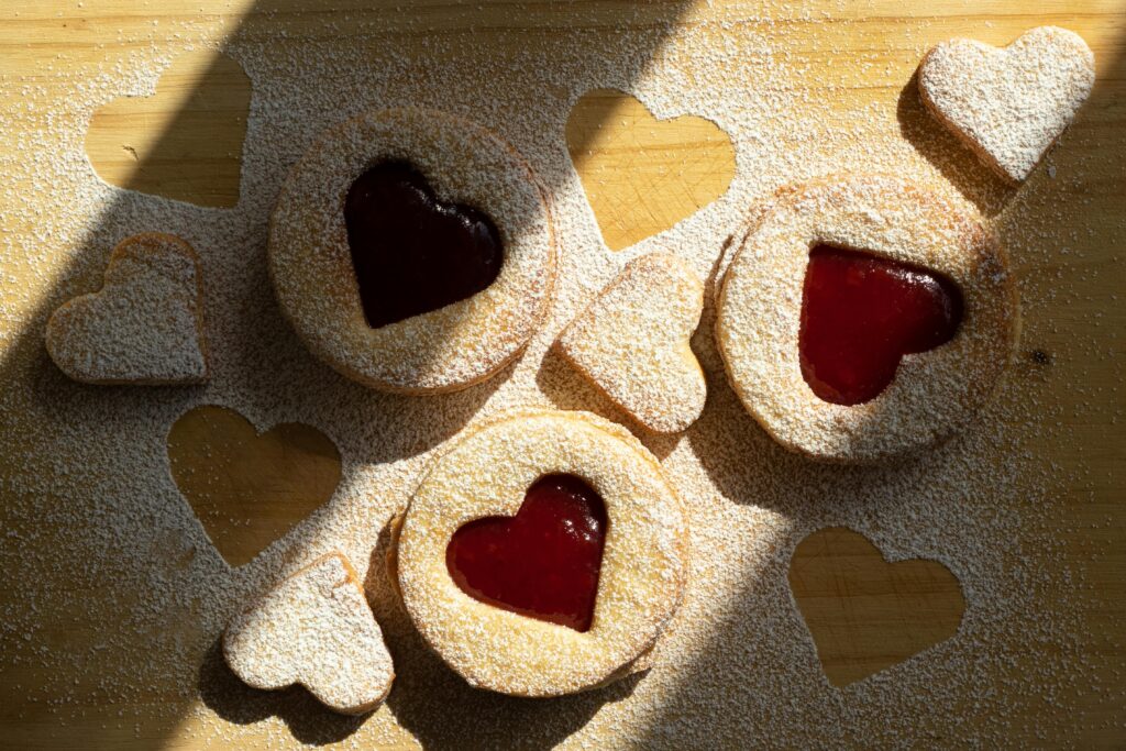 Delicious heart-shaped jam cookies on a powdered sugar-dusted wooden surface.