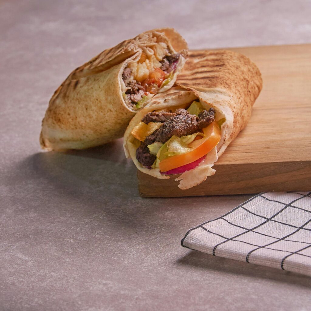 Tasty beef shawarma wrap with fresh veggies on a wooden cutting board, ready to eat.