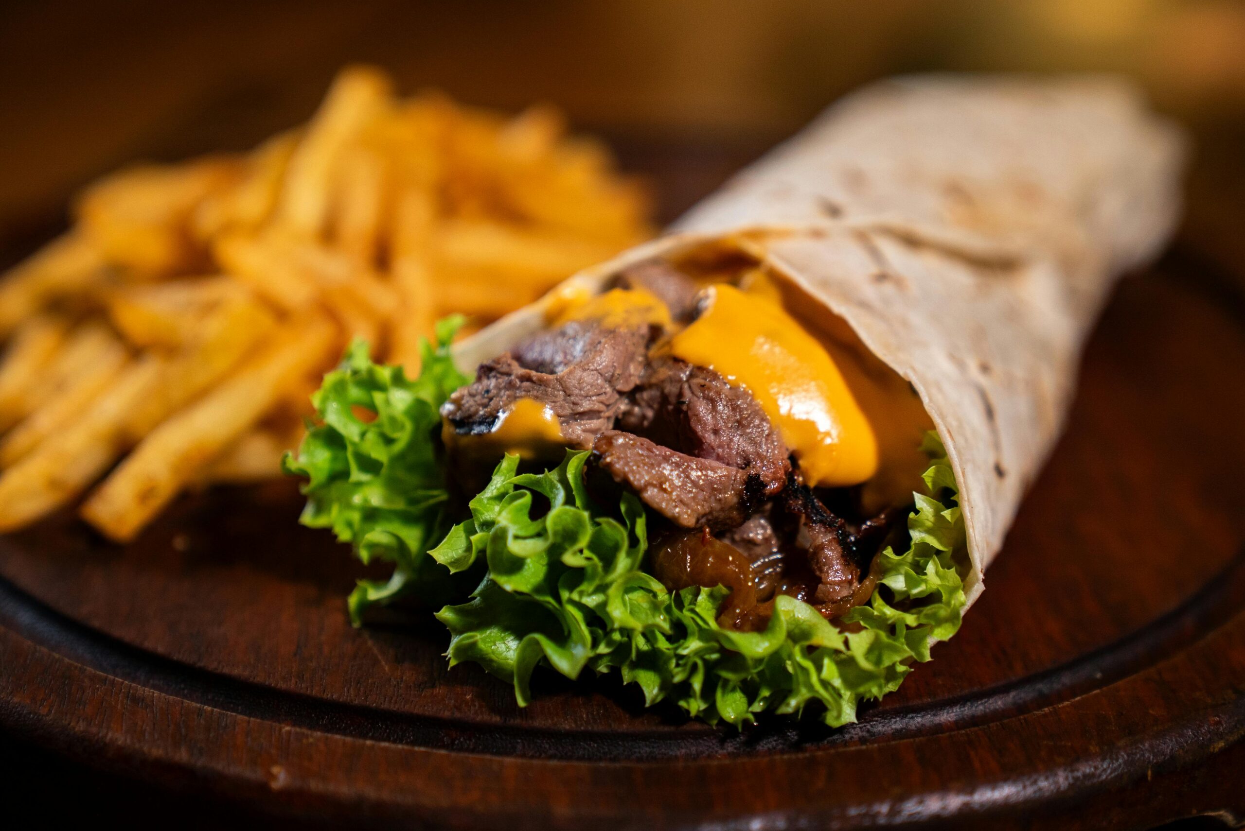 Savory beef wrap with cheese and lettuce served with crispy french fries on a wooden plate.